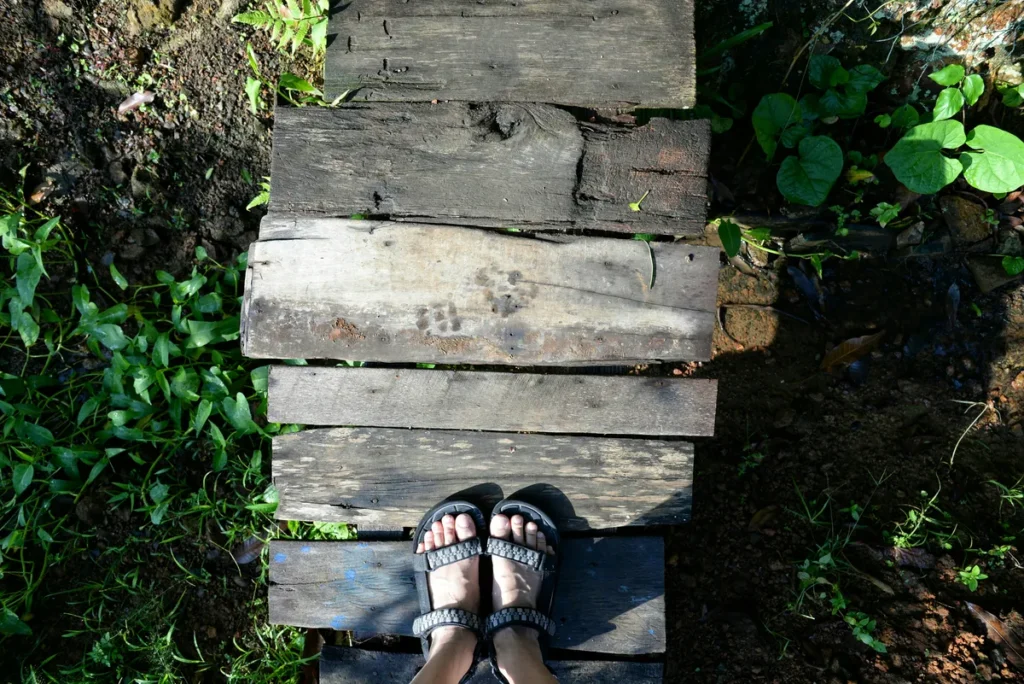 Feet standing on a wooden path representing small steps towards goals and personal growth