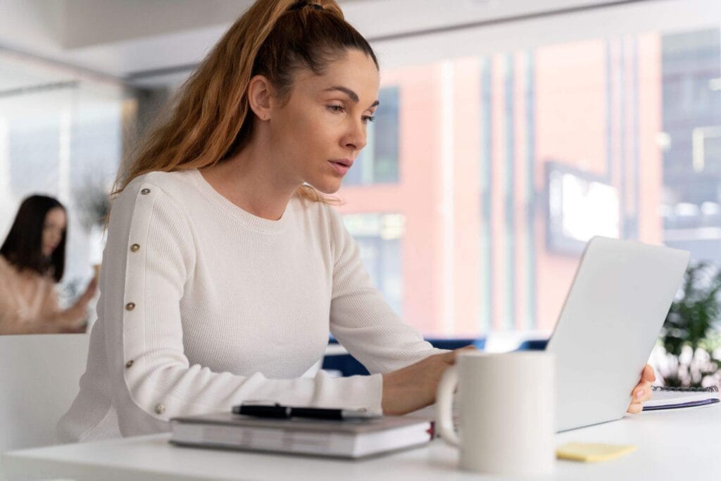 Woman with ADHD focusing on work, using a laptop in a modern office.