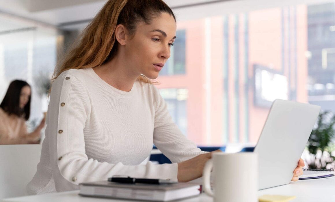 Woman with ADHD focusing on work, using a laptop in a modern office.