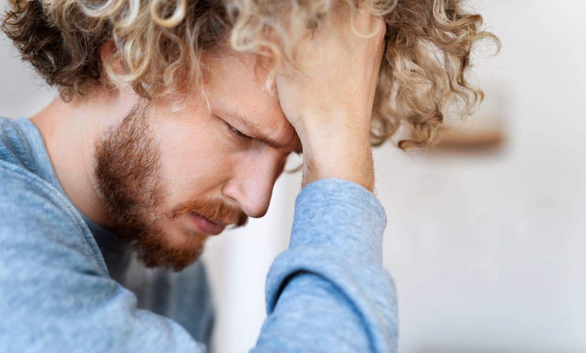 A man sitting with his head resting on his forehead, illustrating the emotional impact of managing shame