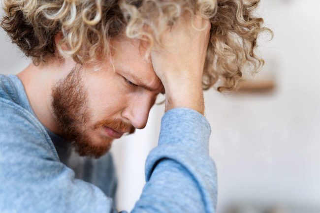 A man sitting with his head resting on his forehead, illustrating the emotional impact of managing shame