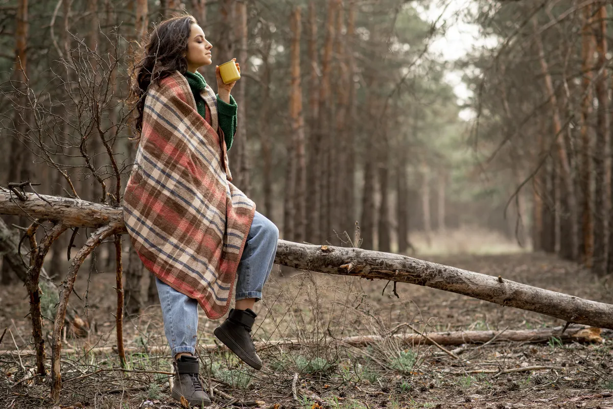 Woman enjoying a quiet moment with a cup of tea in the woods while reflecting on boundaries and self-care