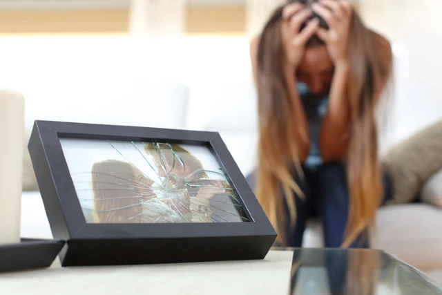 Adult holding their head beside a broken screen, representing emotional overwhelm