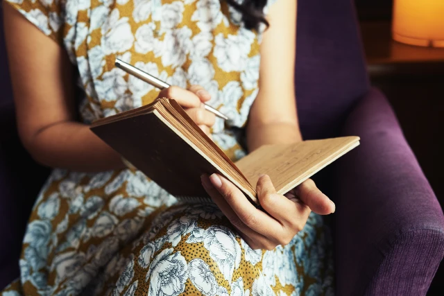 A woman in a dress writing in a journal, symbolising the personal and transformative benefits of journalling.
