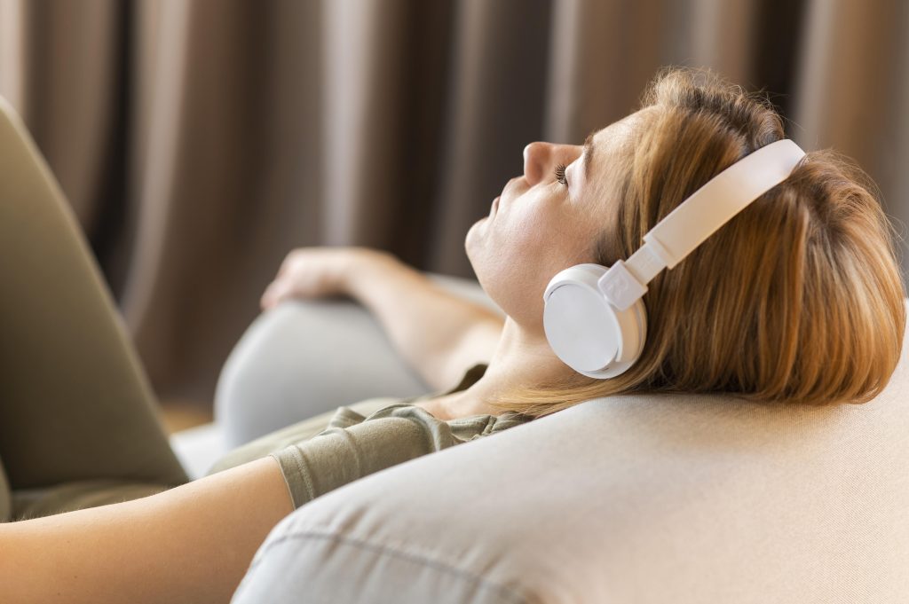 Woman resting on a sofa wearing headphones, eyes closed