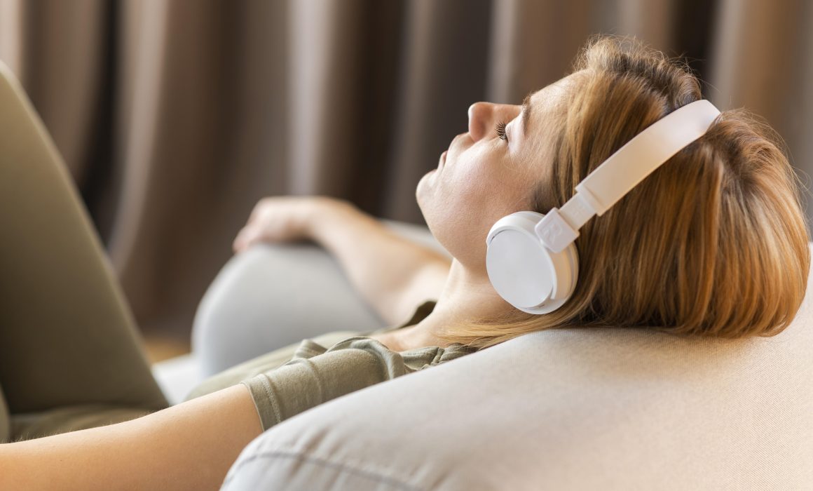 Woman lying on sofa with headphones, using hypnotherapy for ADHD management