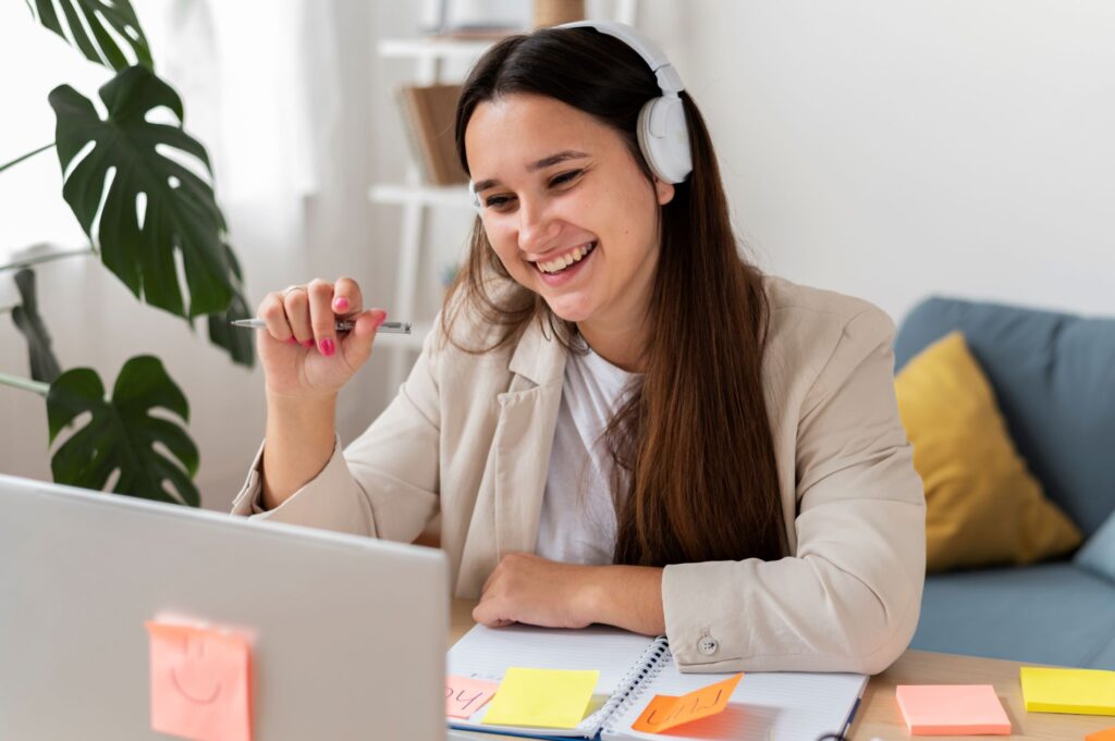Smiling woman at work on a laptop with a notebook and sticky notes appearing organised