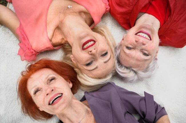 Three smiley mature woman on the ground facing upwards supporting each other