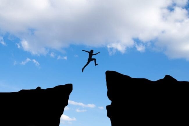 man jumping through gap in cliffs signifying reaching your goals