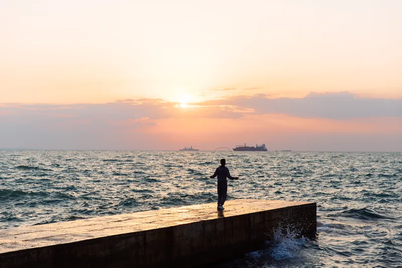 Person standing on a jetty looking towards the sea at sunset