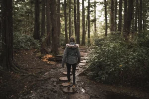 Woman walking across stepping stones through a woodland path during a life transition