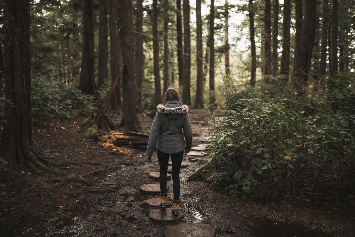 Woman walking across stepping stones through a woodland path during a life transition