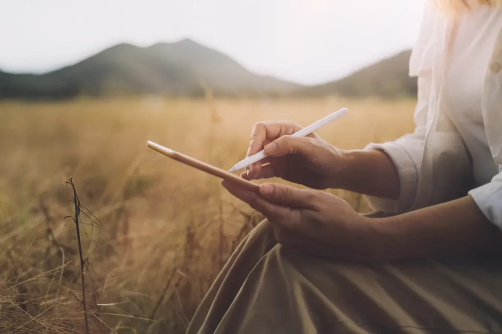 Person writing in a journal while reflecting on goals and personal growth outdoors