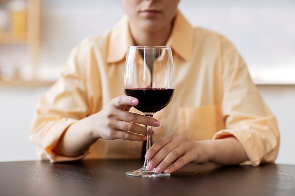 Women in an orange shirt drinking red wine considering stopping drinking alcohol