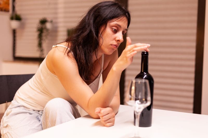Stop Drinking Alcohol Blog for RTT woman looking sad sitting at a table contemplating drinking wine