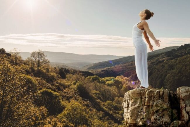 A woman stands on a cliff with arms open, embracing freedom and confidence. A powerful image symbolising mindset shifts, self-belief, and breaking negative patterns.