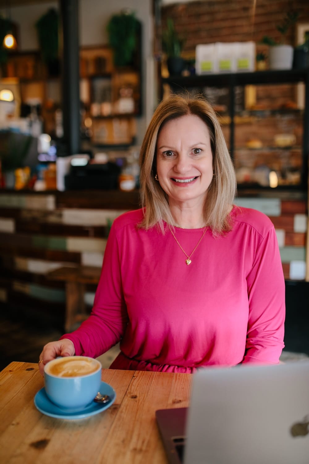 Carol Gordon, a counsellor based in Inverurie, sitting in a cosy café with a laptop and a cup of coffee, smiling warmly.