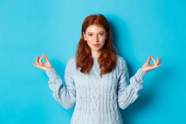 Red-haired woman in a blue blouse practicing mindfulness with hands in a yoga pose, symbolising overcoming perfectionism and inner peace.