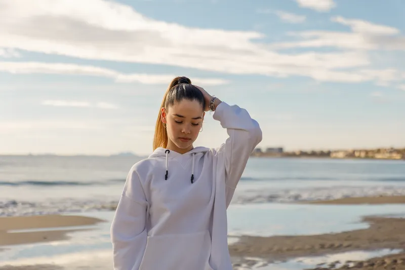 Woman walking on the beach with her hand on her head, replaying embarrassing moments in her mind