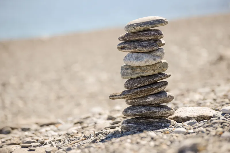 A tall stack of pebbles balanced carefully on a pebble beach against a pale sky