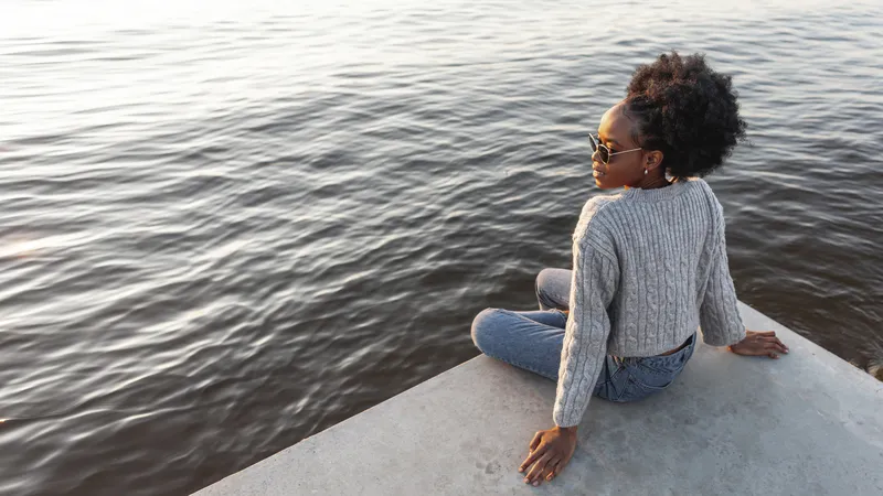 Woman sitting beside the sea, looking out across the water in quiet reflection
