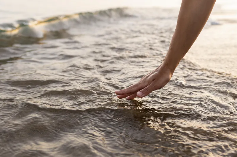 Hand touching the surface of the sea in soft shimmering light