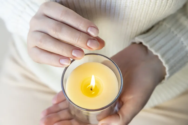 Close up of hands gently cradling a small lit candle in warm soft light