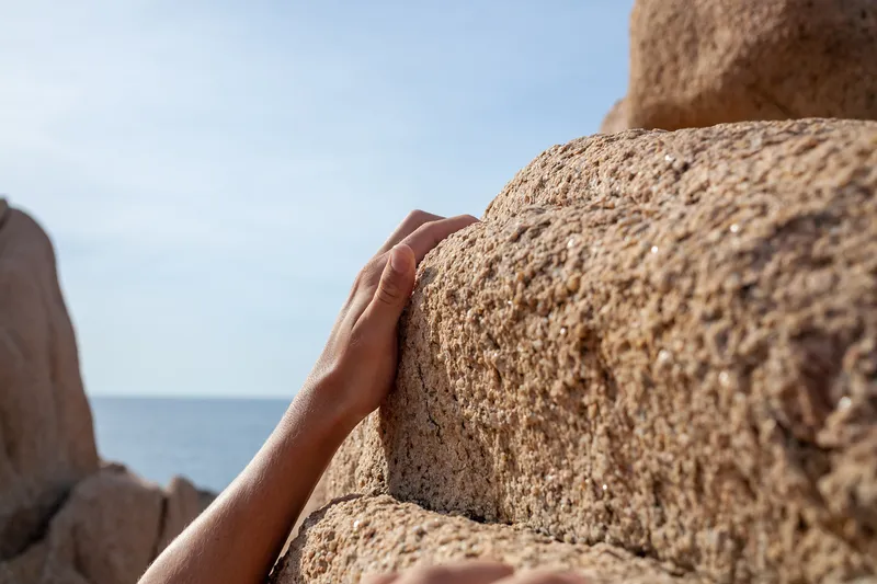 Close up of hands gripping the edge of a sandy rock face by the sea