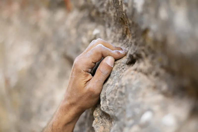 Close up of a hand gripping tightly onto a rocky cliff face