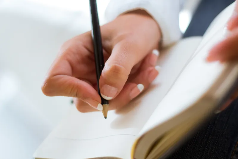 notebook resting on knees outdoors Close up of a hand writing in an open