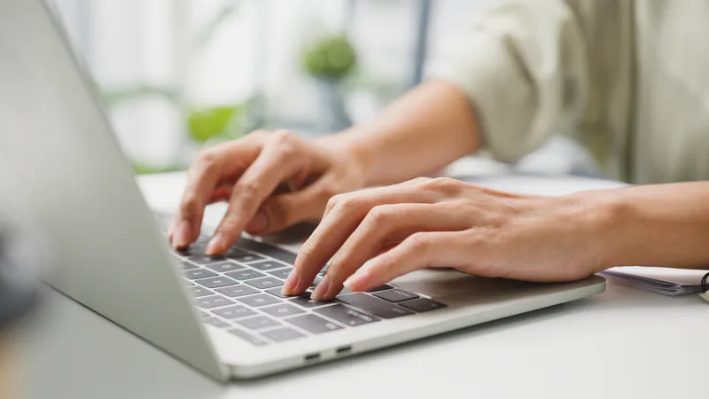 Close up of hands typing purposefully on a laptop keyboard