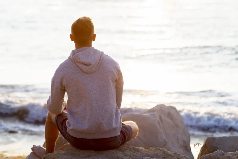 Man sitting on a rock looking out to sea thoughtfully