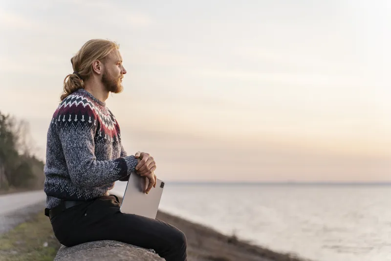 Man sitting on rocks by the sea, looking out at the horizon in quiet reflection