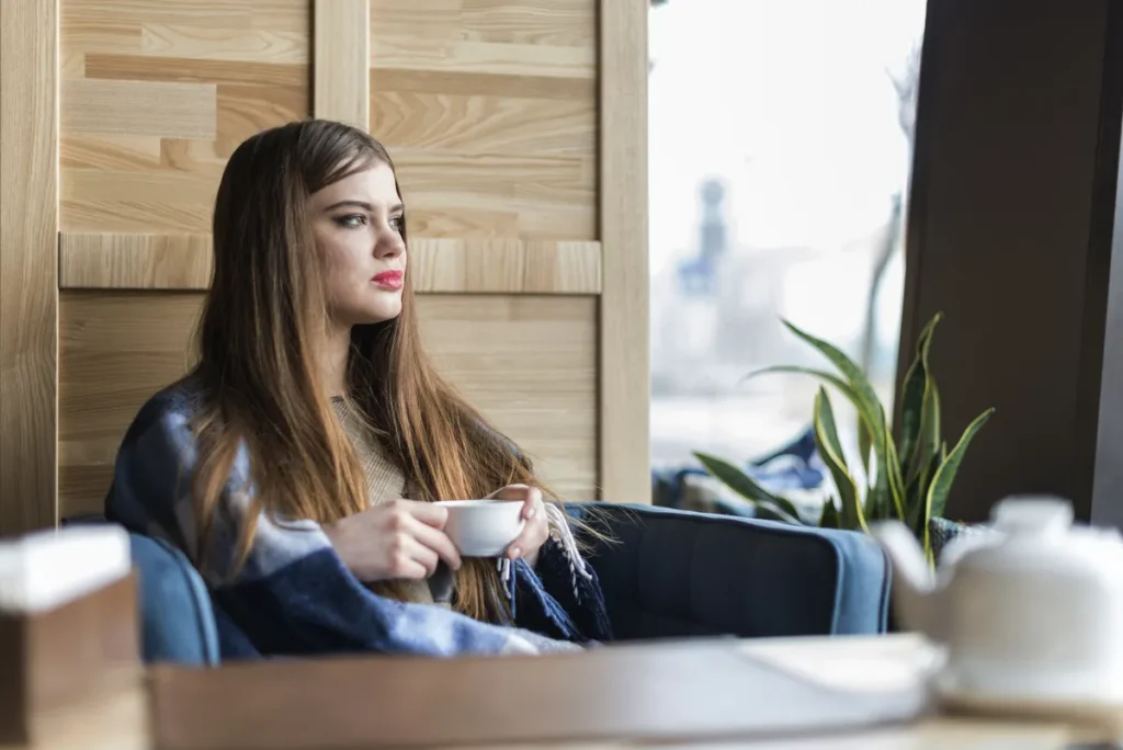 Woman sitting thoughtfully by a window with a cup of tea